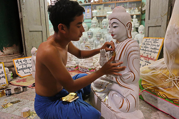 Mandalay statue shop man pasting gold foil on Buddha statue